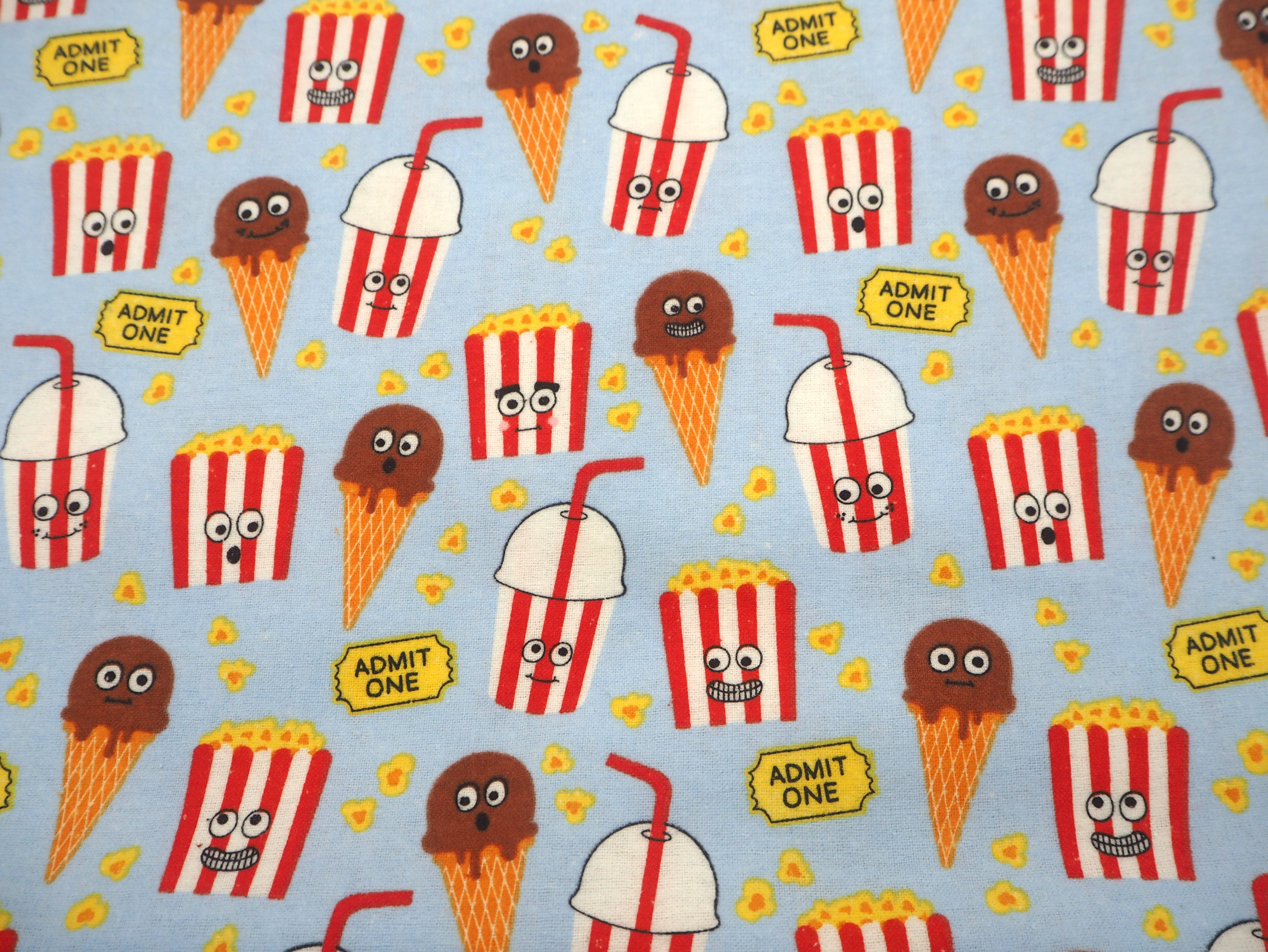 Fabric view of A Sack Of Wheat, featuring images of movie tickets, popcorn & ice-creams on soft blue flannelette, 100% cotton fabric