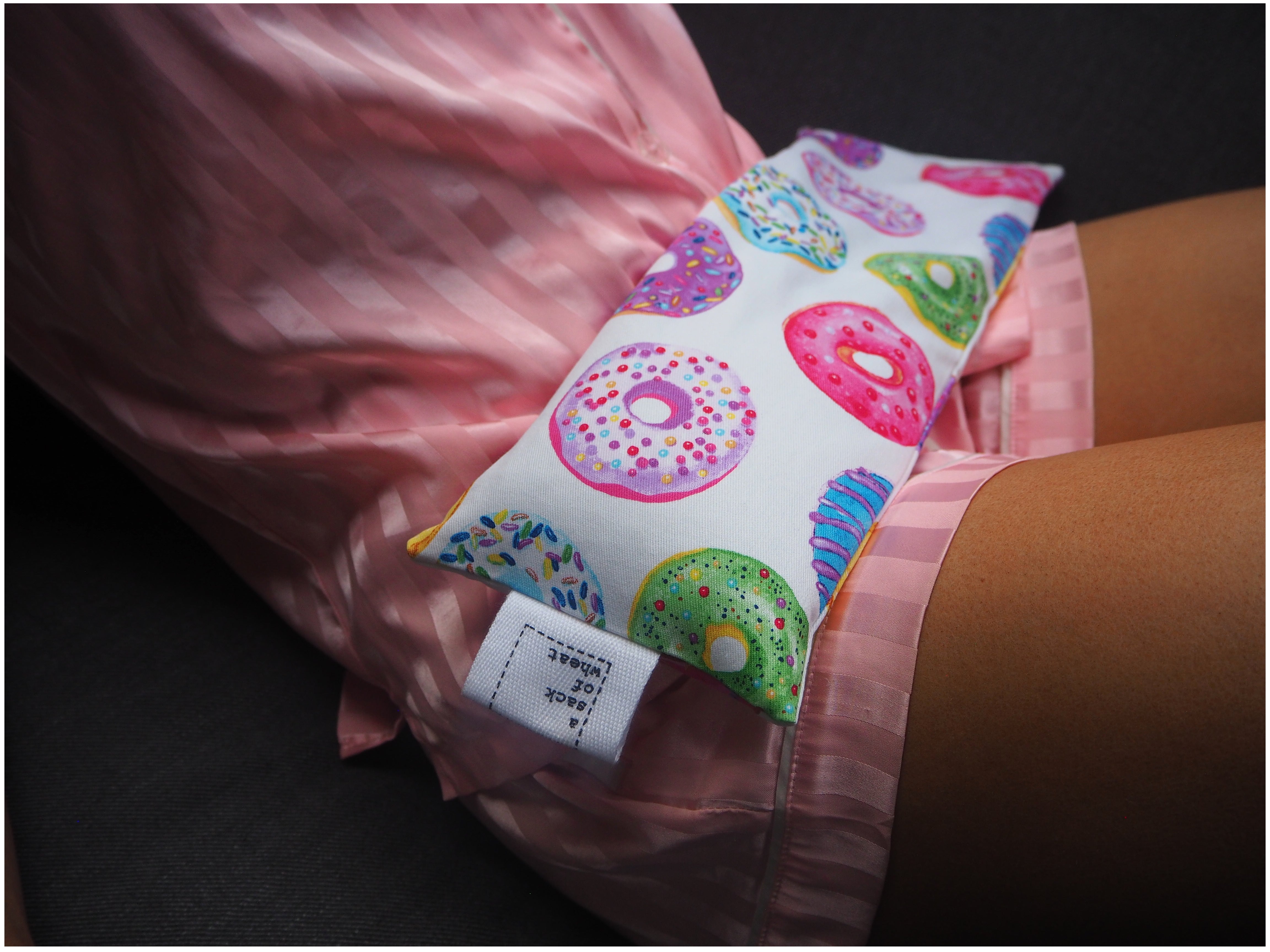 Colorful donut-patterned wheat bag wrapped resting on girls lap wearing pink pajamas 