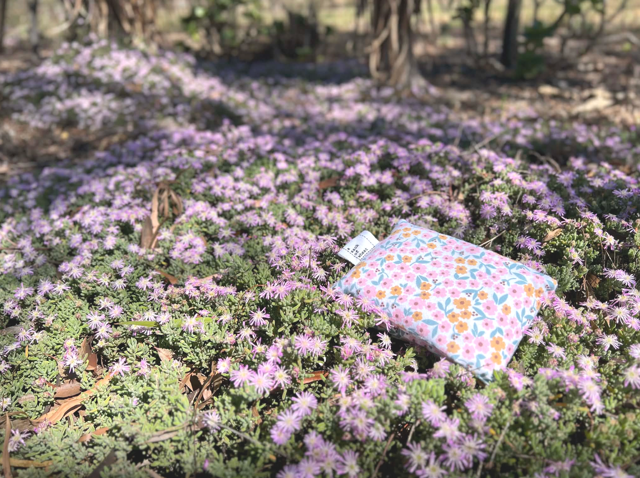 Floral-patterned wheat bags on a bed of pink flowers in a natural setting