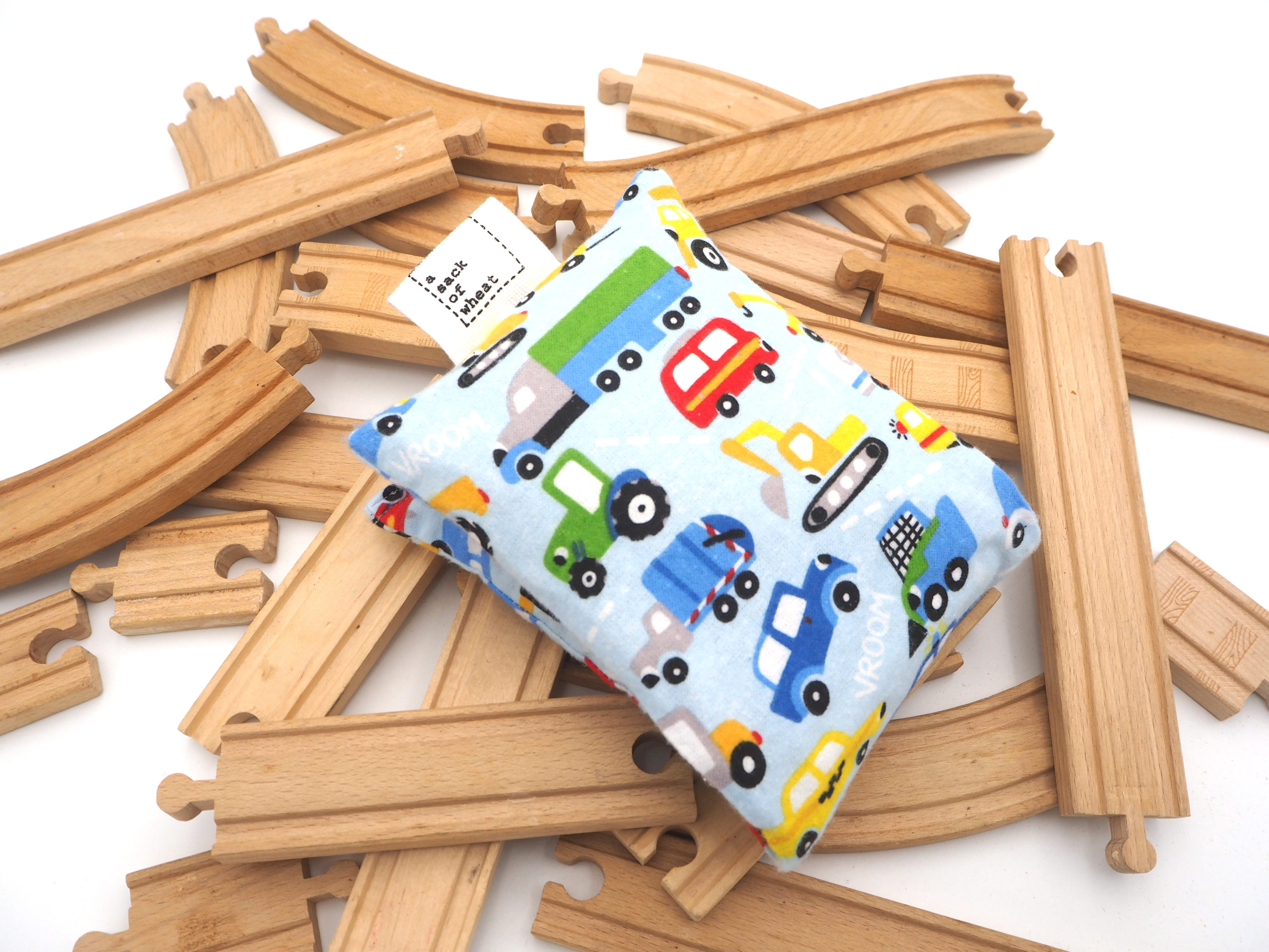 Folded wheat bags with toy cars and trucks on the fabric on a pile of train tracks